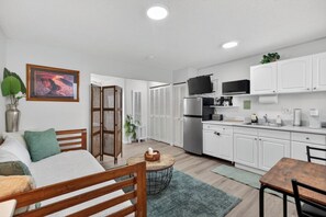A modern kitchen with white cabinets, a refrigerator, microwave, and a dining area with a table and chairs. - Cabana Waikiki Walk to Waikiki Beach With Free Parking Sleep for 4! (Honolulu)