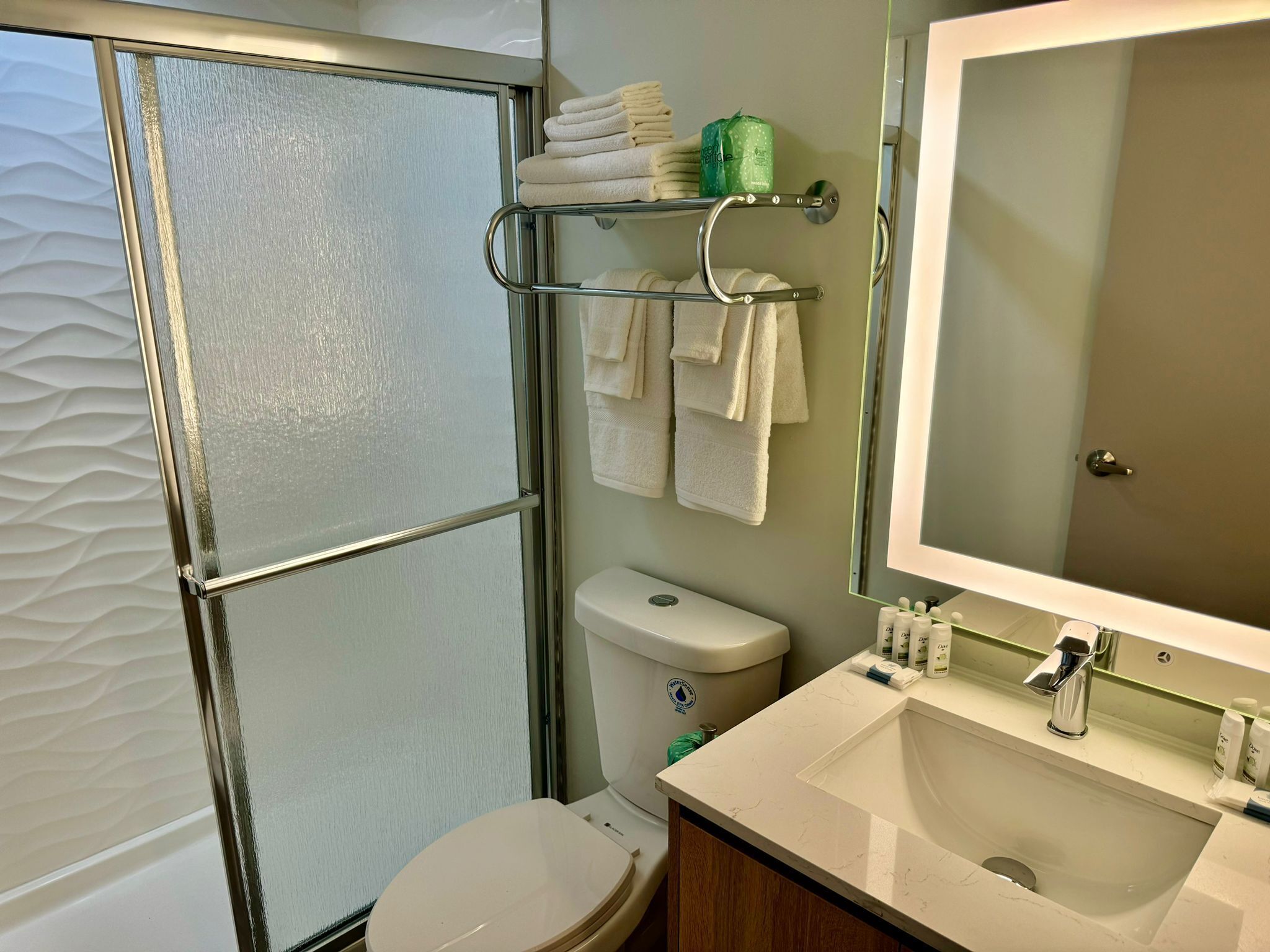 A bathroom with a glass shower enclosure, a toilet, a sink with a mirror, and a towel rack with folded towels.