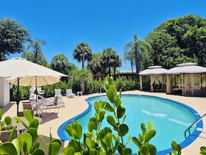 A swimming pool with lounge chairs and umbrellas, surrounded by greenery and trees. - Cozy One Bedroom Suite with Two Double Beds In the Heart of Boynton/Delray Beach (Boynton Beach)