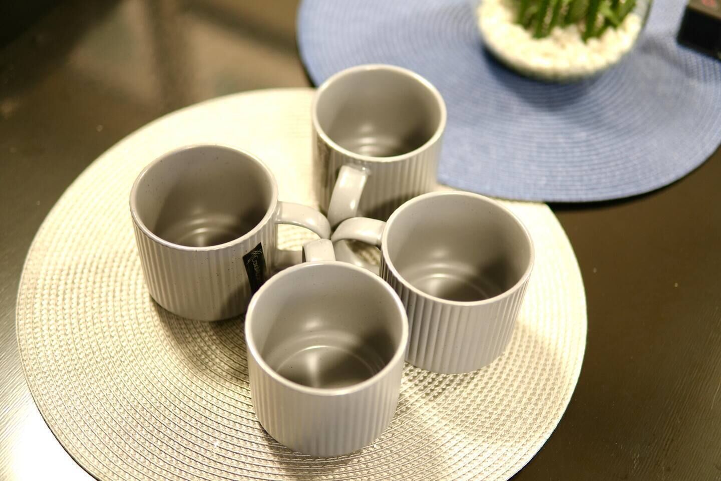 Four white ceramic cups arranged on a textured round mat.