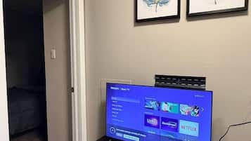 A television on a black stand with a remote control, a wall-mounted picture frame, and a door leading to another room.