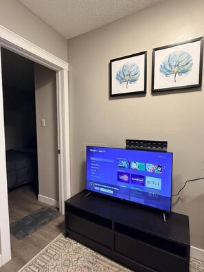 A television on a black stand with a remote control, a wall-mounted picture frame, and a door leading to another room.