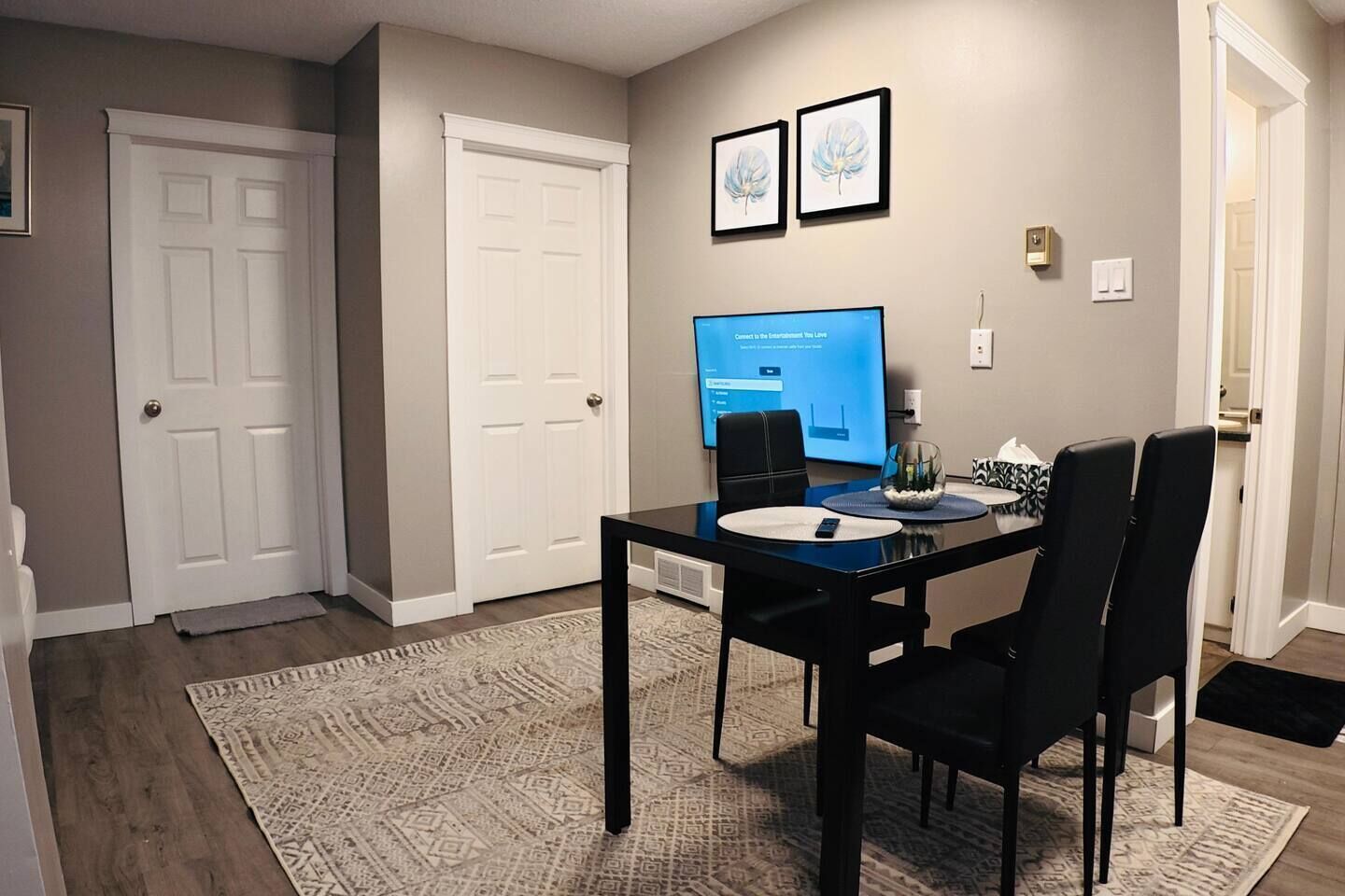 Un espace repas comprenant une table, des chaises, un téléviseur à écran plat et un tapis à motifs.