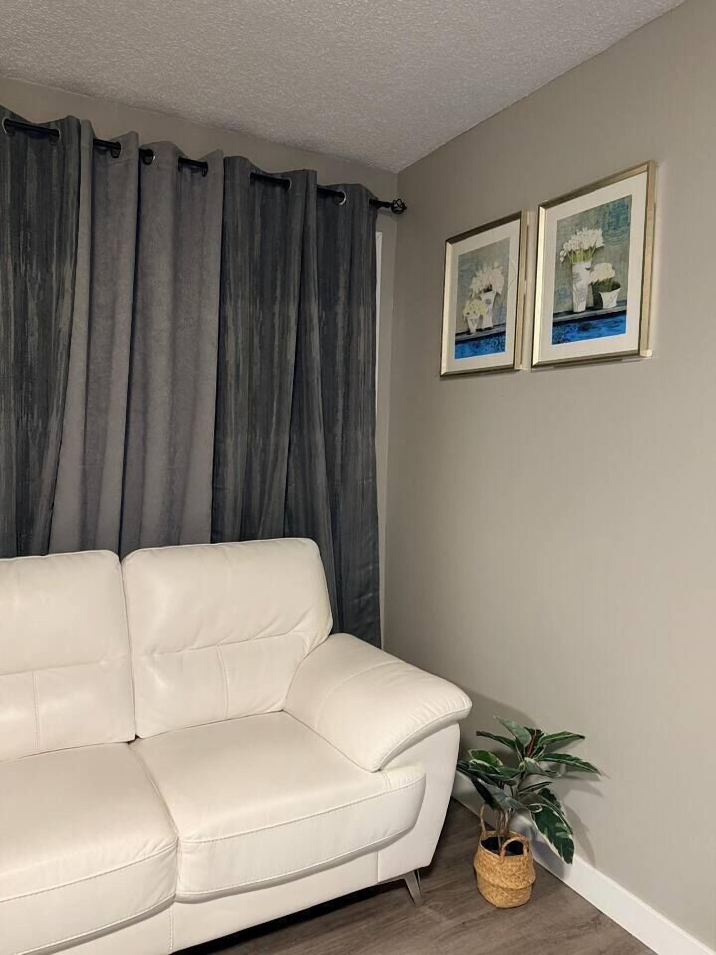 A living room with a white leather sofa, grey curtains, and two framed pictures on the wall.