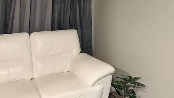 A living room with a white leather sofa, grey curtains, and two framed pictures on the wall.