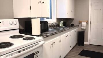 Une cuisine avec des meubles blancs, une cuisinière, un four à micro-ondes et une poubelle noire.