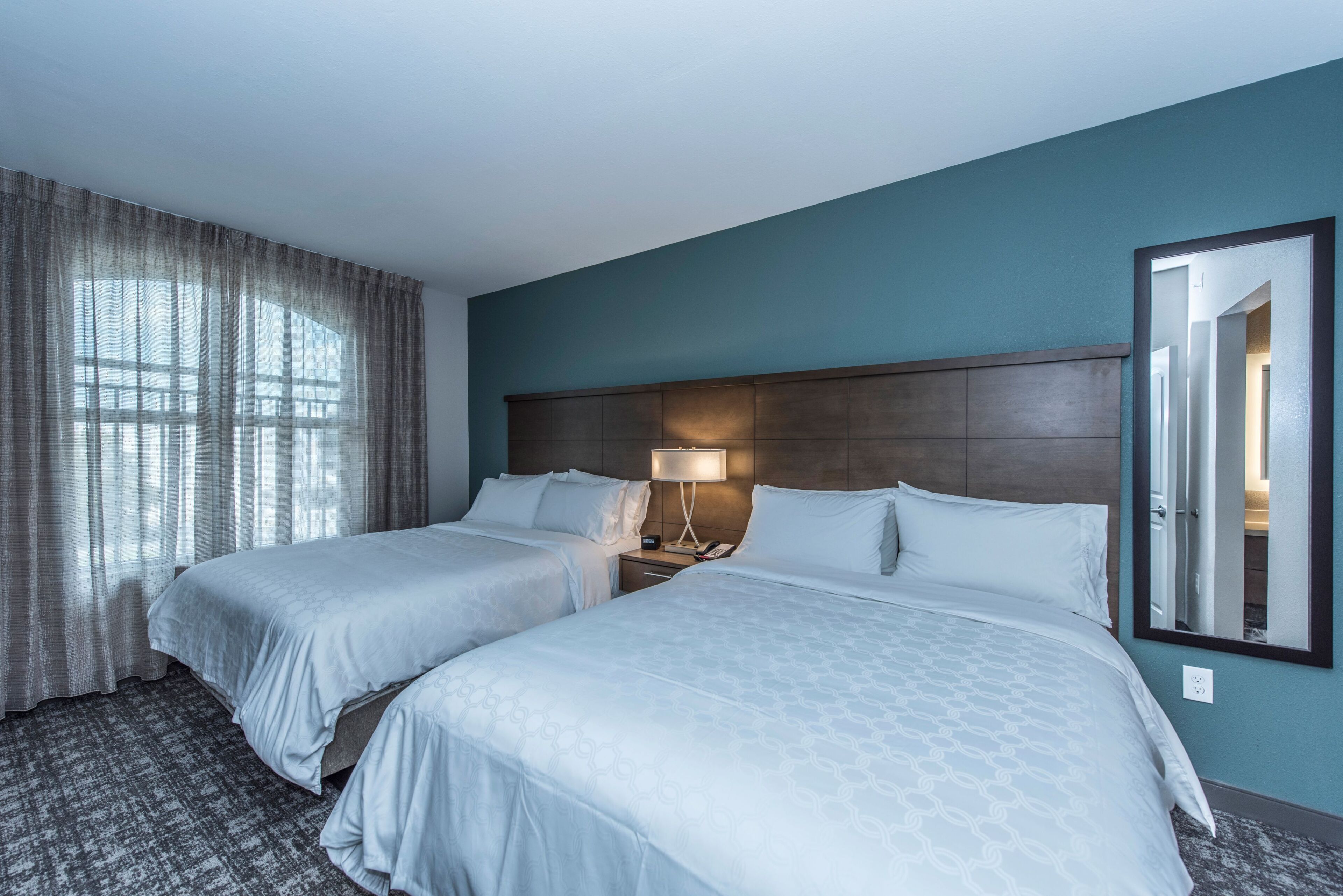 A hotel room with two beds, a nightstand with a lamp, and a large mirror.