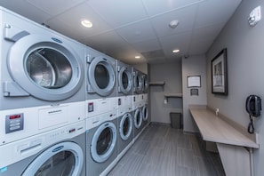 A laundry facility with multiple washing machines, a trash bin, a phone, and a framed notice on the wall.