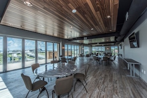 A spacious conference room with a large round table surrounded by chairs, large windows offering views of a bridge and highway, and a wooden ceiling with recessed lighting.