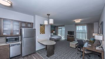 Une chambre d’hôtel de taille réduite, équipée d’une kitchenette, d’un lit, d’un bureau et d’une télévision.