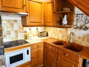 Una cocina con armarios de madera, microondas integrado, tostadora y lavabo.