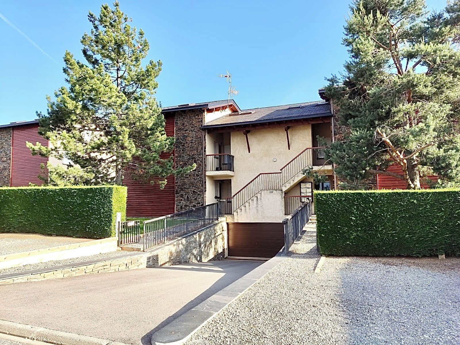 A building with a stone facade, a balcony, and a gravel driveway.
