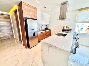 A modern kitchen with a large island, stainless steel appliances, and a view of the city through the window. - Depto Mazatlán Golden View by Interhome (Mazatlán)