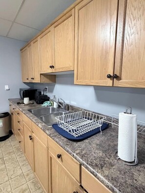 Una cocina con armarios de madera, encimera de granito, pileta de acero inoxidable, escurreplatos y un dispensador de toallas de papel.
