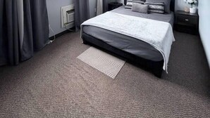 A bedroom with a bed, a nightstand, a lamp, a window with curtains, and a radiator.