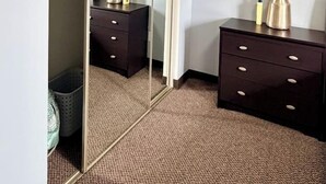 A hotel room with a mirrored closet, two dark wooden nightstands, and a carpeted floor.