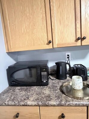 Una cocina con armarios de madera, un microondas negro, una cafetera y una taza de vidrio sobre la encimera.