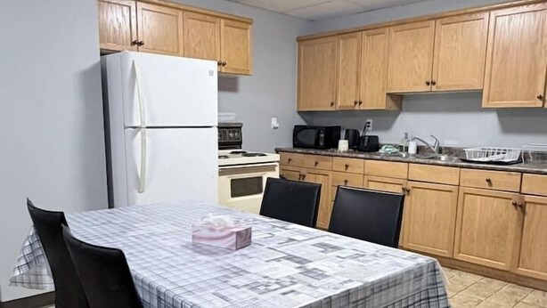 A compact kitchen with wooden cabinets, a white refrigerator, and a dining table set with chairs.
