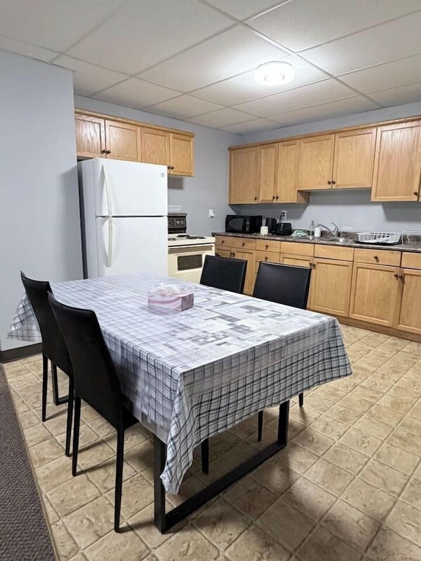 A compact kitchen with wooden cabinets, a white refrigerator, and a dining table set with chairs.