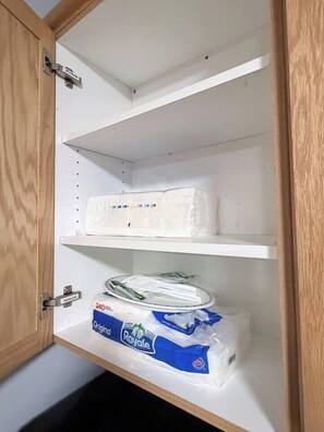 A cabinet with three shelves; the bottom shelf has a package of Royale toilet paper.