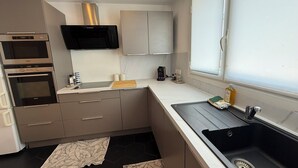 Cuina moderna amb electrodomèstics integrats, una finestra amb persianes i un lavabo de tauletera negra.