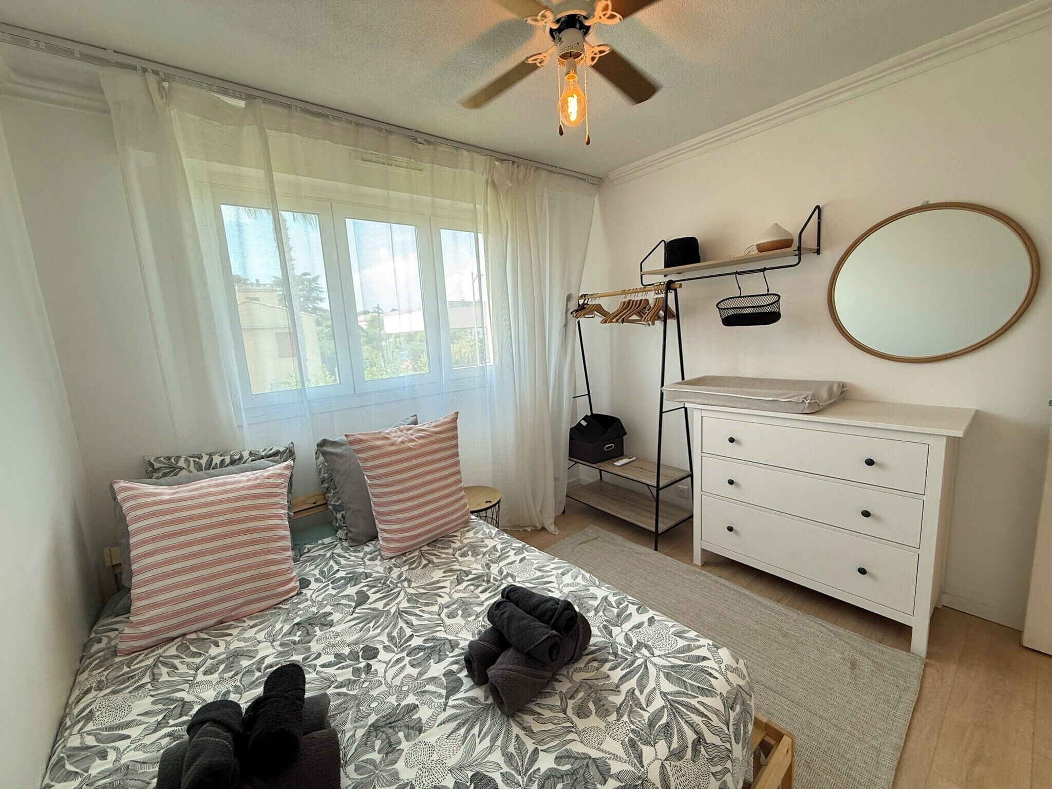 A bedroom with a bed, a dresser, a mirror, and a ceiling fan.