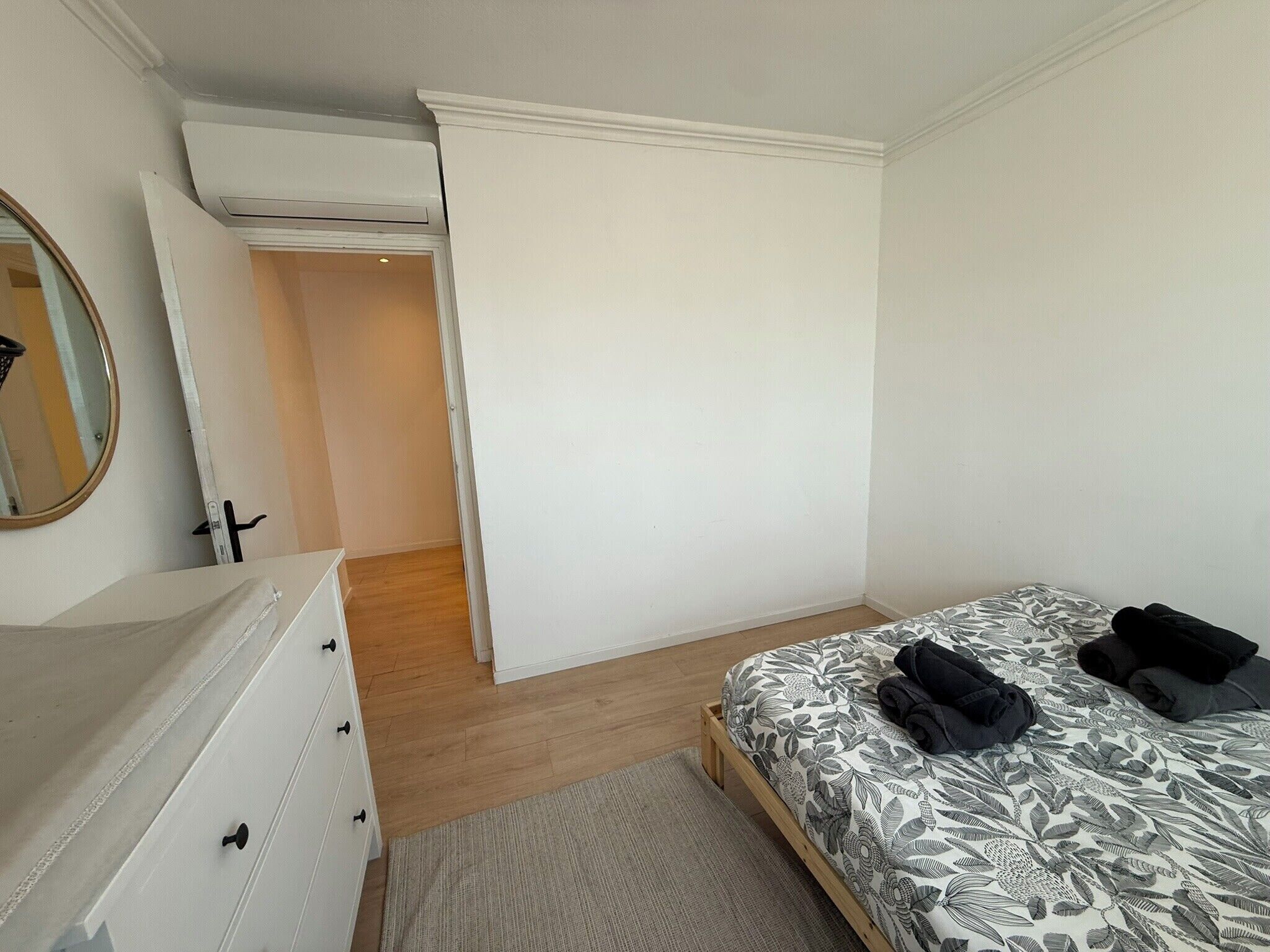 Un dormitorio con cama, cómoda, espejo y puerta que da a otra habitación.