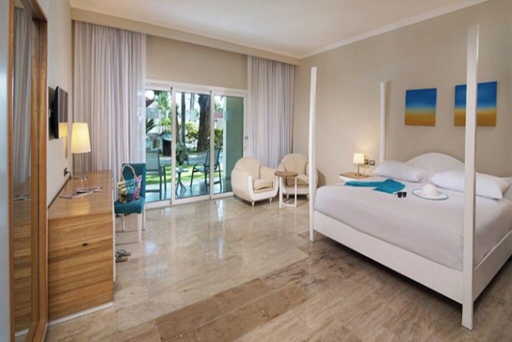 A hotel room with a large bed, a desk, a chair, and a view of the outdoors.