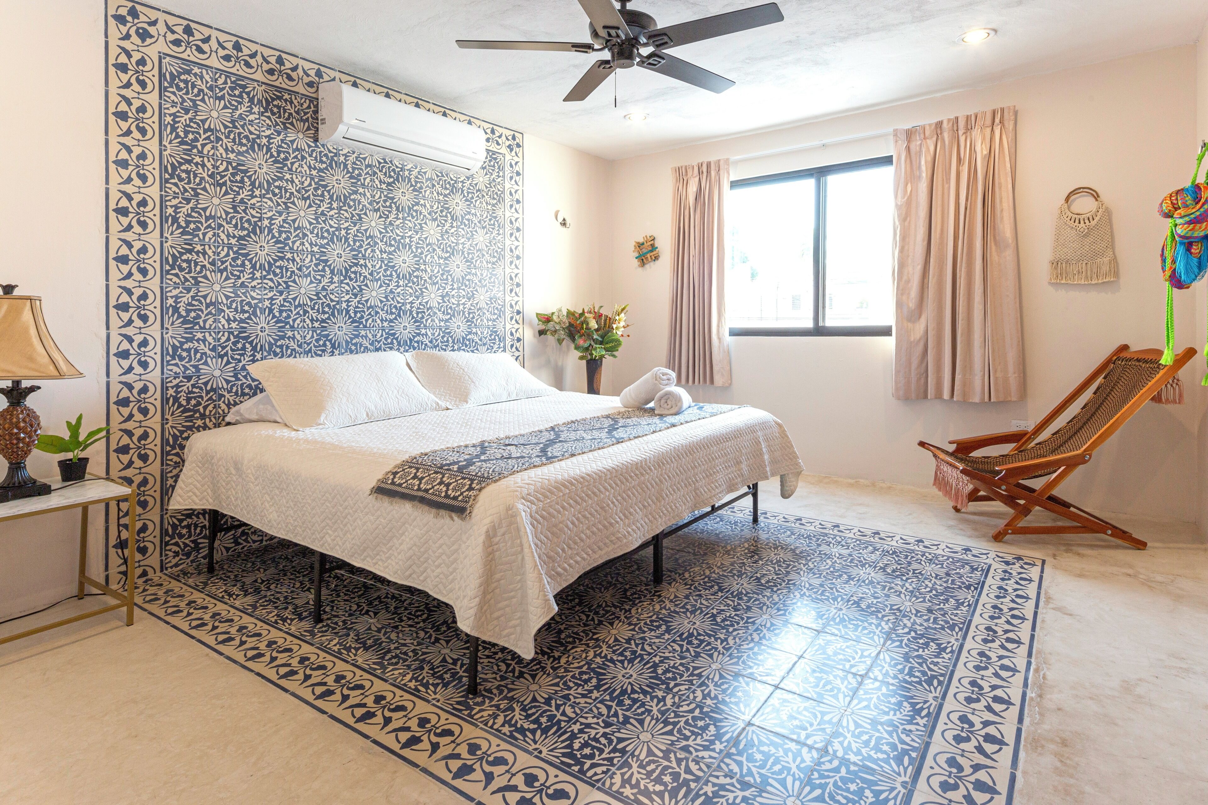 Une chambre à coucher comprenant un lit, un ventilateur de plafond, une fenêtre avec des rideaux, une chaise et un climatiseur fixé au mur.