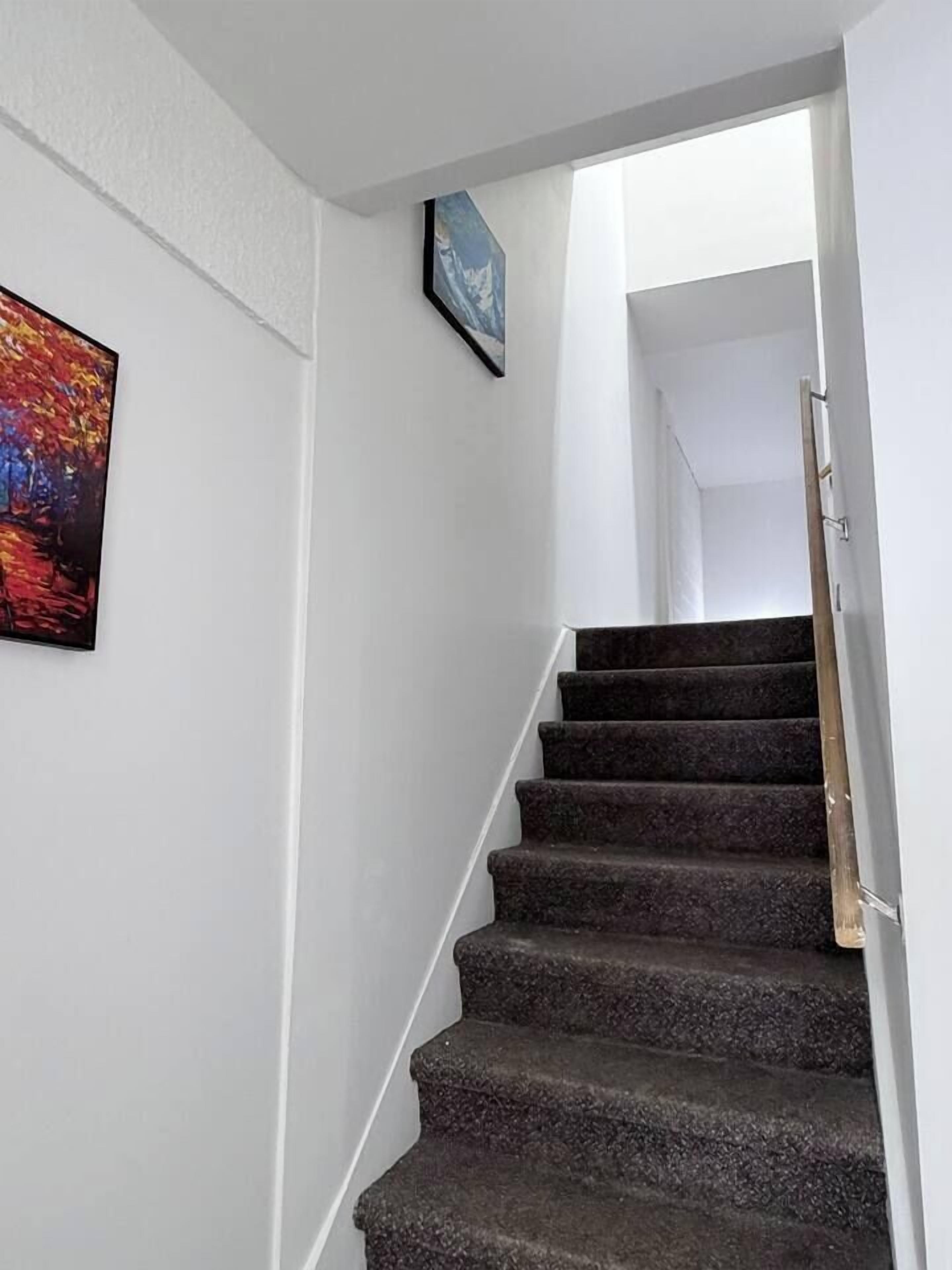 Un escalier avec une rampe, des murs blancs et deux œuvres d’art encadrées.
