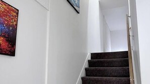 Una escalera con barandilla, paredes blancas y dos cuadros enmarcados.