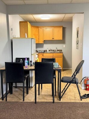 A compact kitchen with wooden cabinets, a refrigerator, a sink, and a dining area with chairs.