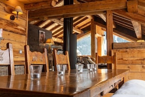 A wooden interior with a dining table set for four, wooden chairs, and a large window offering a view. - Chalet, 150m from ski slopes, 3rd floor, view panoramic, terrace, fireplace or stove, 250m² (Champagny-en-Vanoise)