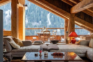 A cozy cabin interior with a wooden deck, a sofa, a table with drinks, and a view of snow-covered mountains. - Chalet, 150m from ski slopes, 3rd floor, view panoramic, terrace, fireplace or stove, 250m² (Champagny-en-Vanoise)