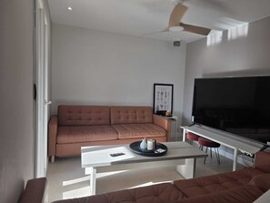 Ein Wohnzimmer mit einer Couch, einem Couchtisch, einem Fernseher und einem Deckenventilator.