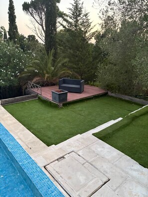 A backyard with a swimming pool, a wooden deck, and a seating area with a bench and a planter. - Villa Saint Raphael in peaceful Valescure (Golf course and beach nearby) (saint raphael)