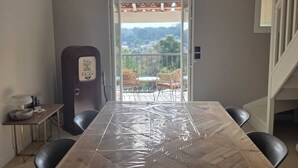 Ein Zimmer mit einem großen Tisch, der mit Folie abgedeckt ist, einem Deckenventilator und Blick durch eine offene Tür auf einen Balkon mit Stühlen.