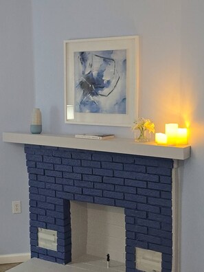 Una llar de foc de maó blau amb una prestatgeria blanca, un quadre abstracte emmarcat i espelmes enceses.