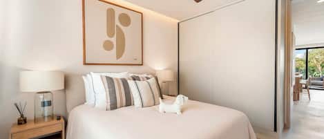 A modern bedroom with a large bed, a ceiling fan, a framed abstract artwork, and a view of the outdoors.