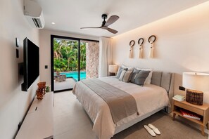 Een moderne slaapkamer met een groot bed, een plafondventilator, een televisie en uitzicht op een zwembad.