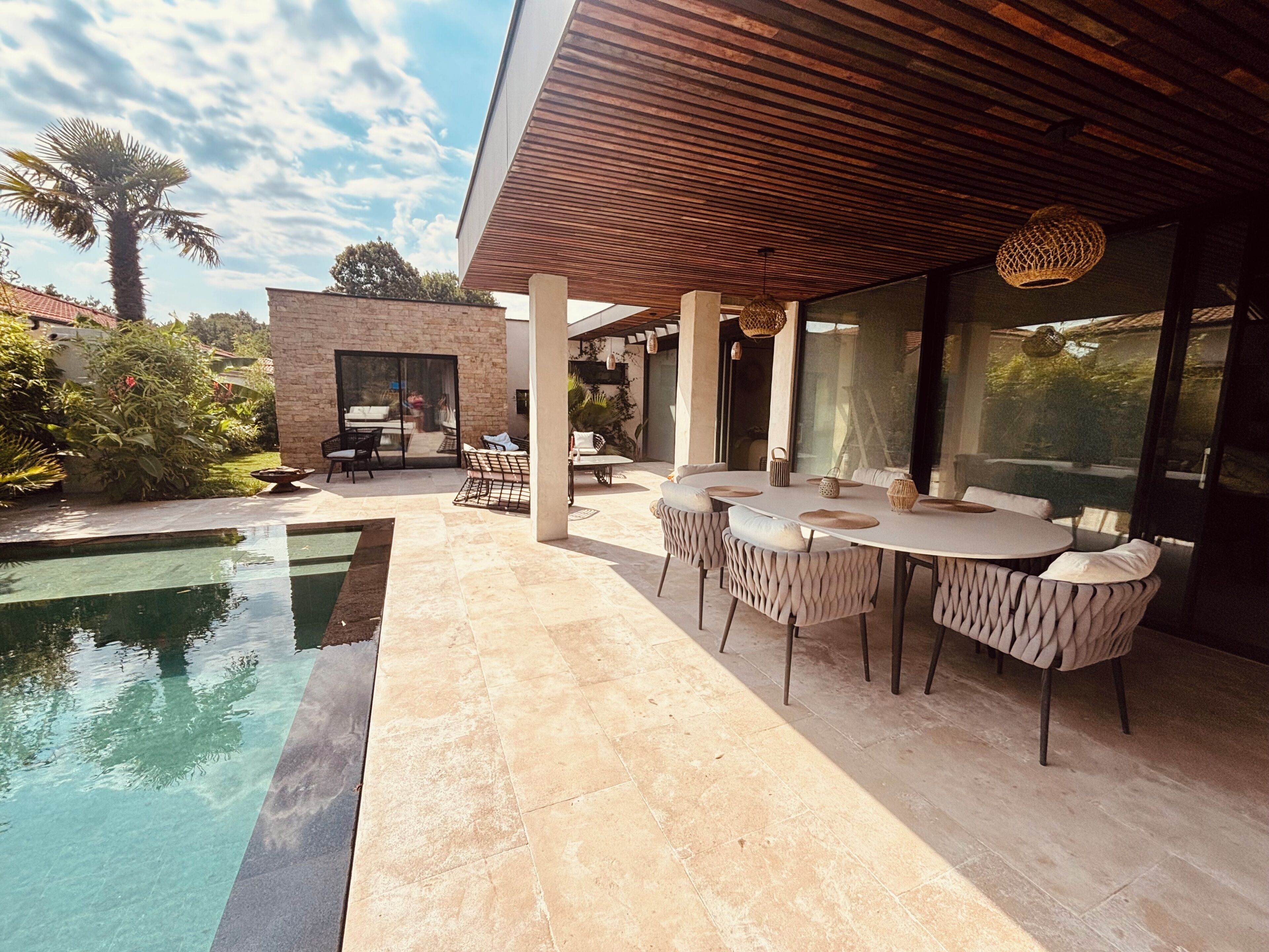 Une terrasse extérieure moderne avec une piscine, un espace repas et un mur en pierre.