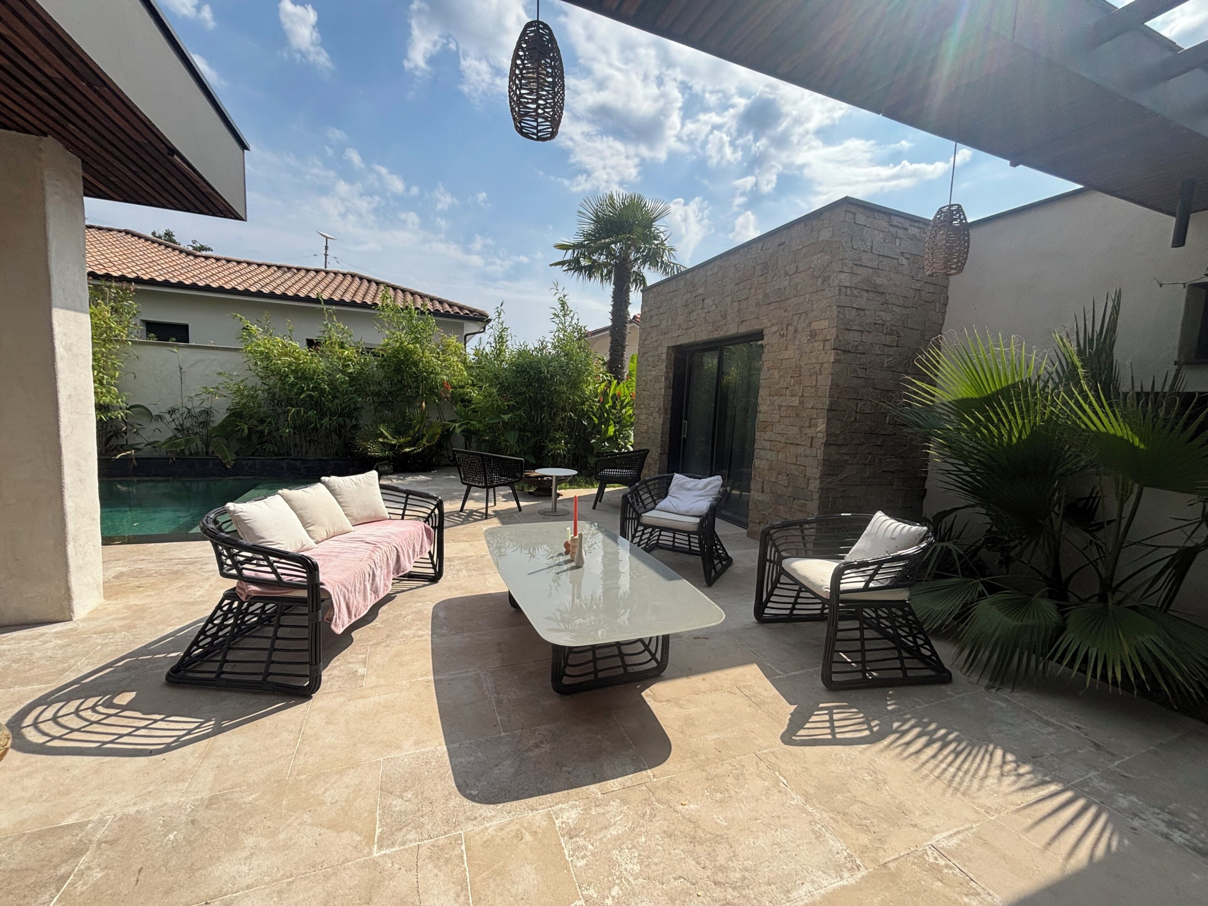 Um pátio externo com mesa de vidro, cadeiras de vime e um sofá.