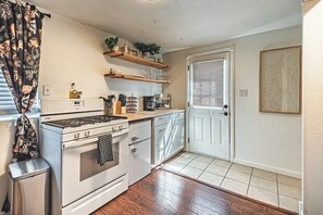 A kitchen with a stove, oven, and countertop. There are wooden shelves above the counter and a door with a patterned panel. - Cozy Studio Near Garden of the Gods - Fenced Yard (Colorado Springs)