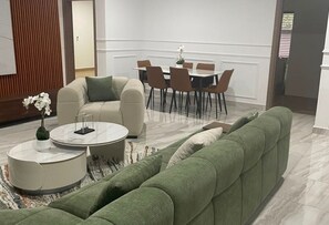 Una sala de estar moderna con un sofá verde, una mesa de centro redonda y una zona de comedor con mesa y sillas.