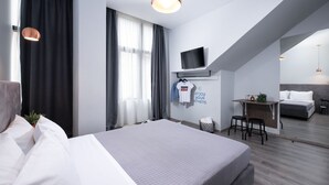 A modern hotel room with a large bed, a desk with a chair, a television, and a small balcony.