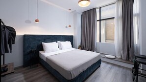 A modern bedroom with a large bed, a bedside table, a hanging light fixture, and a window with curtains.
