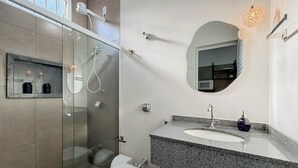 Une salle de bain moderne avec une douche à parois de verre, des toilettes, un lavabo avec un miroir et un luminaire au plafond.