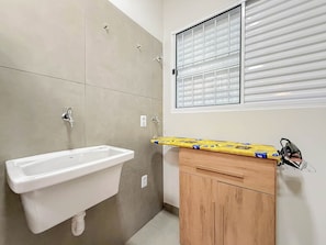 A bathroom with a white sink, wooden cabinet, and a window with blinds.