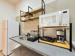 A compact kitchenette with a refrigerator, microwave, coffee maker, and a dish rack.