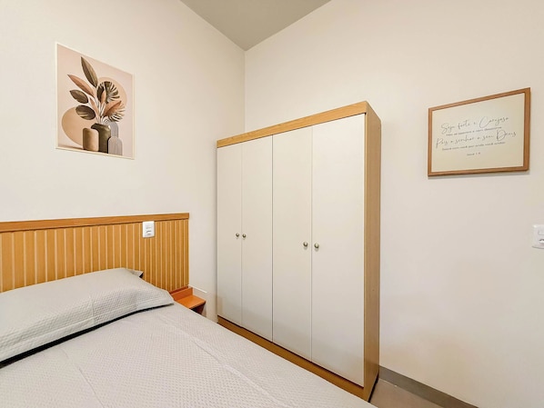 A bedroom with a bed, a wardrobe, and two framed items on the wall.